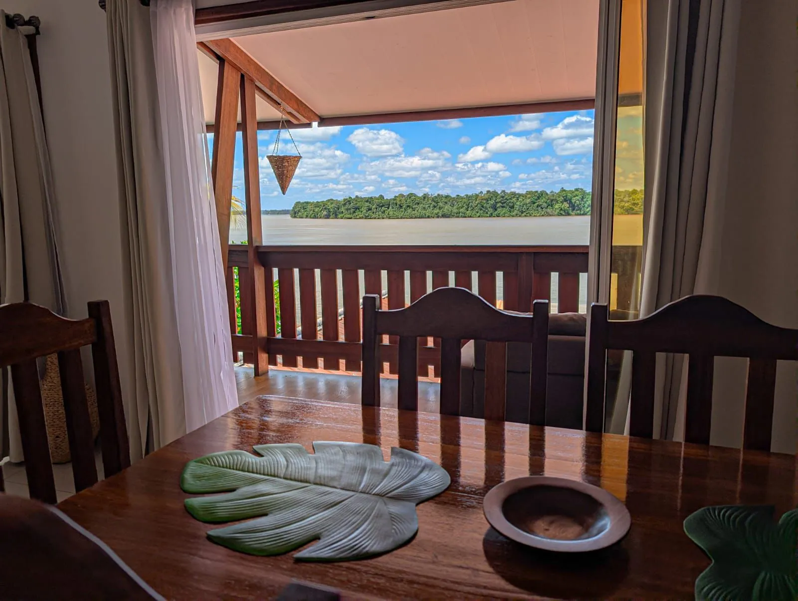 Table en bois devant une baie ouverte sur le balcon et le fleuve Maroni